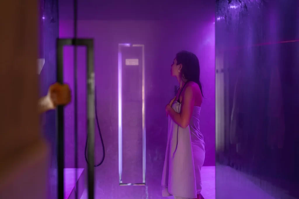 Una donna avvolta in un asciugamano si trova in una stanza illuminata da luce viola.