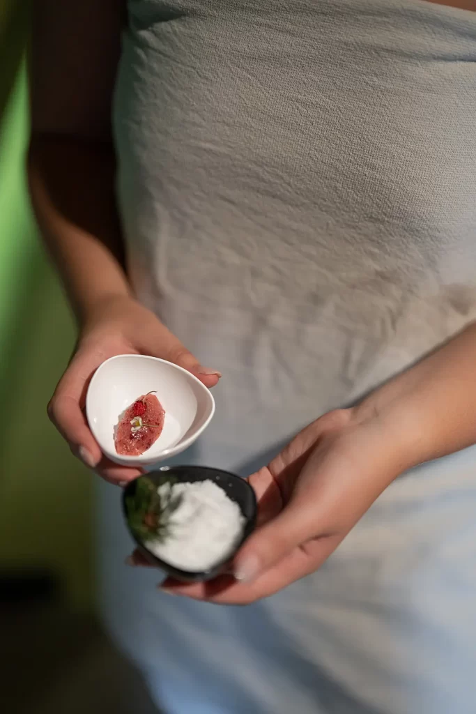 Una persona avvolta in un asciugamano bianco tiene due ciotole con ingredienti per la cura della pelle.