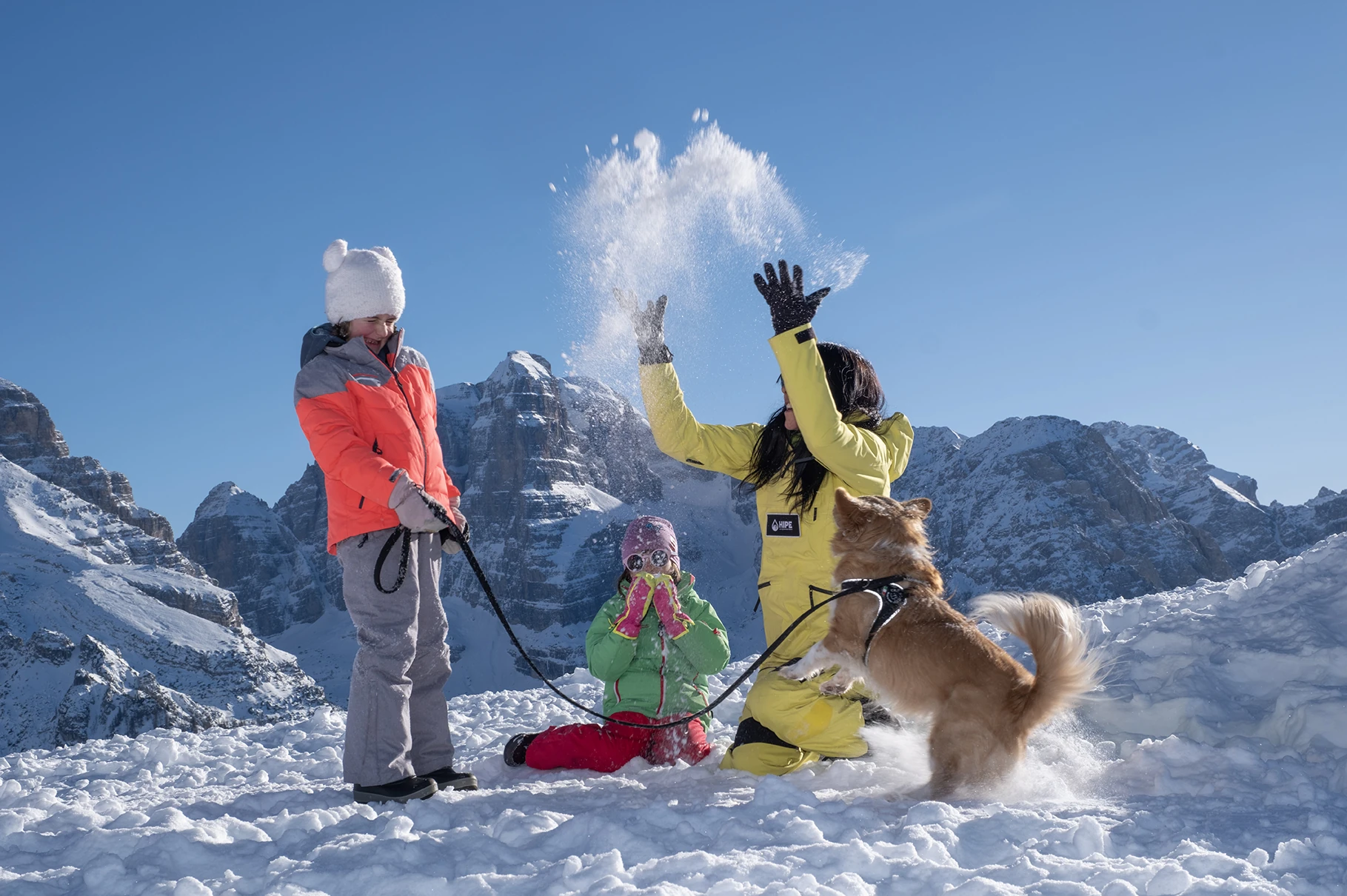 A family with a dog plays in the snow on a mountain.