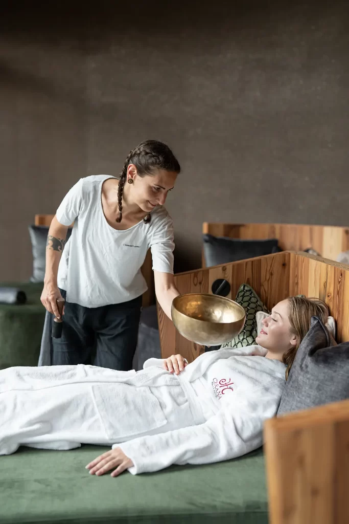 Operatrice esegue una terapia sonora su una donna sdraiata in una spa.