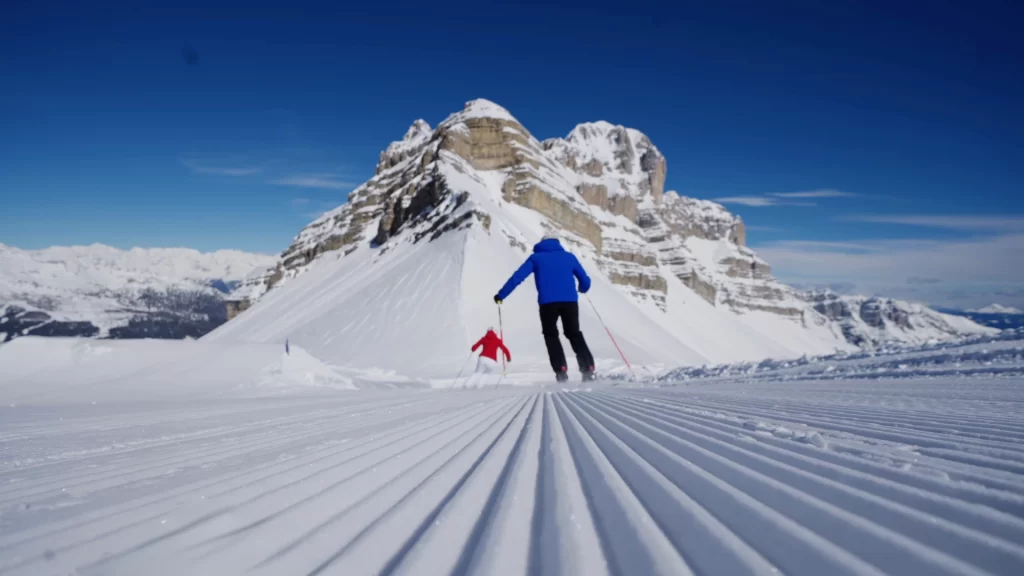 Due sciatori scendono una pista innevata con una montagna sullo sfondo.