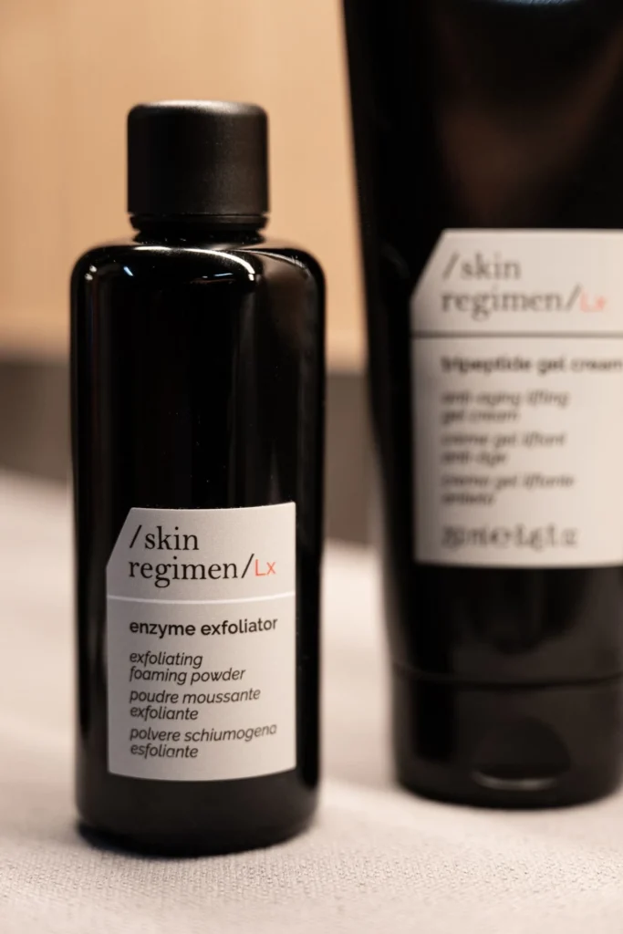 Two black bottles of skin care products with white labels on a soft surface.
